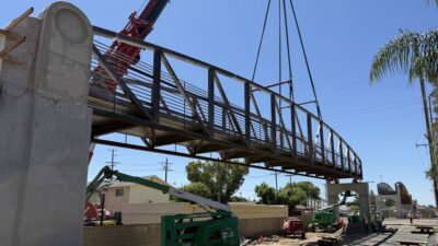 A crane lifts a prefabricated steel bridge section into position during installation. The modular construction approach allowed the bridge to be assembled and erected within a limited construction window.