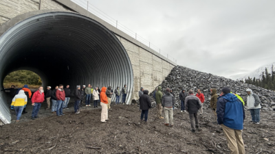 Meeting participants stand inside a large-diameter corrugated steel structural pipe being constructed as a wildlife underpass as part of the Sterling Highway project.